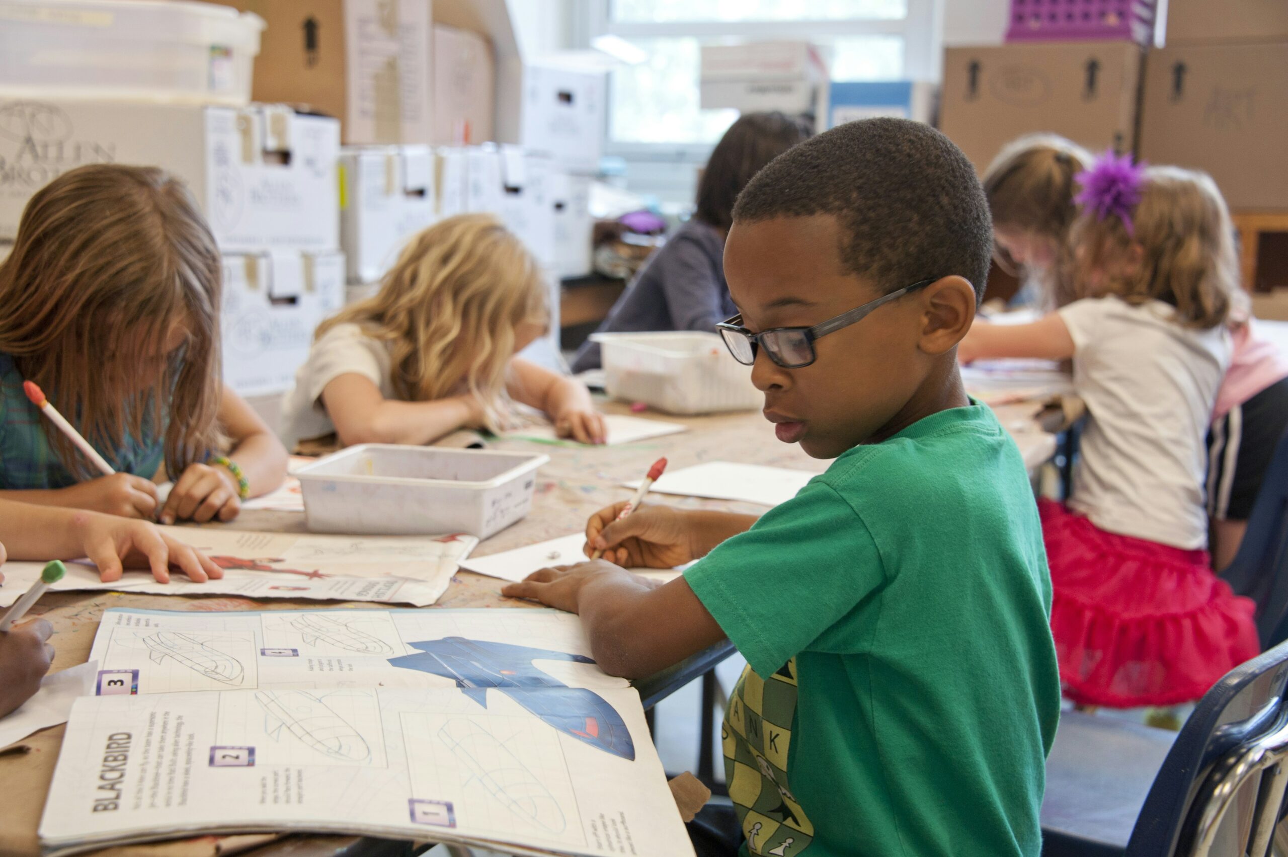 Elementary school students working quietly at a classroom table on drawing and writing activities.
